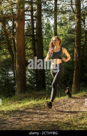 Giovane donna atletica slim che si prepara per una maratona mentre correre attraverso la foresta Foto Stock