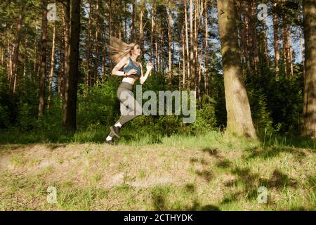 Giovane donna atletica slim che si prepara per una maratona mentre correre attraverso la foresta Foto Stock