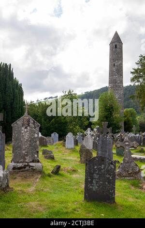 Un cimitero Glendalough con una torre rotonda Glendalough sullo sfondo Foto Stock