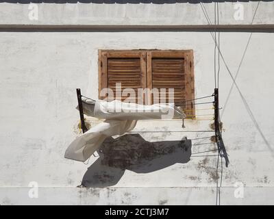 Vecchia finestra marrone di legno su una parete bianca, i vestiti sono asciugati su una corda Foto Stock