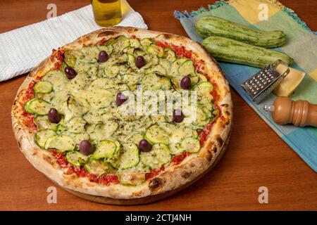 Deliziosa pizza italiana vegetariana, con salsa di pomodori, peperoni, olive e zucchine su sfondo di tavola in legno. Testo in portoghese: Serenità Foto Stock