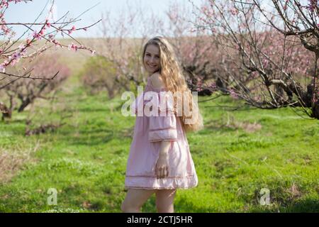 Bella donna bionda in abito rosa cammina attraverso il giardino fiorito Foto Stock