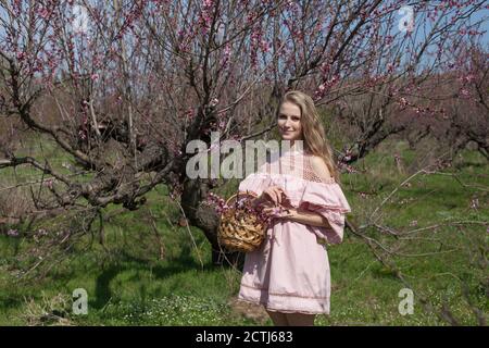 Bella donna bionda in abito rosa cammina attraverso il giardino fiorito Foto Stock