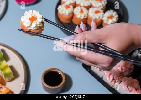 Primo piano di bacchette che prendono parte al sushi roll. Set di deliziosi panini sushi, piatto Foto Stock