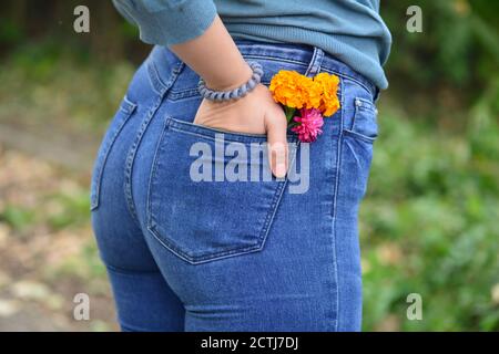 Fiore arancione brillante in jeans blu tascabile di giovane donna in piedi su sfondo natura, primo piano Foto Stock