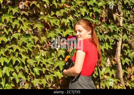 Bella giovane donna con un bouquet di fiori vicino a una parete verde di cespugli. Affari floreali. Spazio di copia. Foto Stock