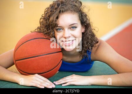 Felice giovane ragazza giocatore di pallacanestro che tiene una palla mentre si trova su un campo all'aperto. Primo piano del ritratto del modello. Foto Stock