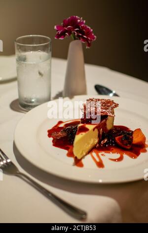 una gustosa fetta di dessert alla cheesecake ricoperta di fragole servita insieme un bicchiere d'acqua Foto Stock