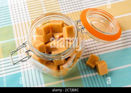 Caramelle fresche di caramello alla vaniglia in un vaso di vetro aperto con clip sopra la tovaglia. Gustosi bonbon mastici fatti di latte e zucchero. Foto Stock