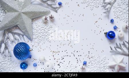 Natale e Capodanno stelle bianche, fiocchi di neve e palline blu di Natale e decorazioni tra scintille su uno sfondo bianco, vista dall'alto, disposizione piatta, copia centro benessere Foto Stock