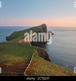Uno scenario di un bel faro che sorge su una splendida scogliera sullo sfondo del mare e illuminato dal sole che tramonta. Neist Point, Isola di Skye, Scozia Foto Stock