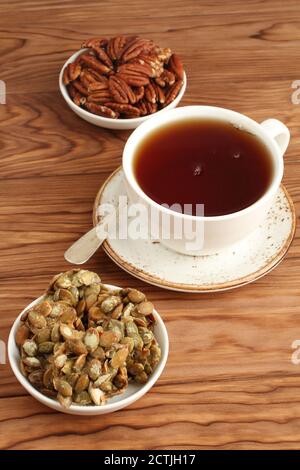 Biscotti di semi di zucca ricoperti di zucchero, noci pecan in una ciotola e una tazza di tè nero su un tavolo di legno. Primo piano Foto Stock