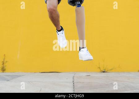 Anonimo sportivo con protesi delle gambe in sneakers che saltano contro il giallo parete Foto Stock
