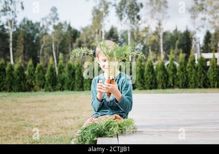 il ragazzo sedette nel suo giardino sorridendo alla sua casa carote Foto Stock