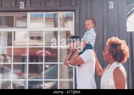 Papà che porta il bambino sulle spalle con la mamma sorridente davanti di grande finestra Foto Stock