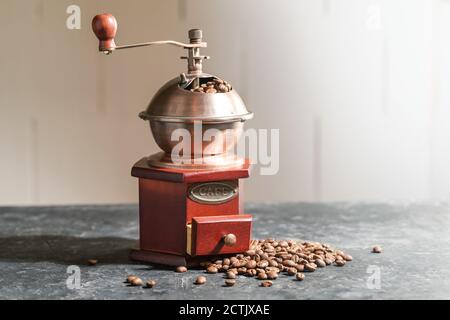 Macinacaffè in legno d'epoca e alcuni chicchi arrostiti su un banco da cucina in ardesia contro una parete luminosa, spazio di copia, fuoco selezionato Foto Stock