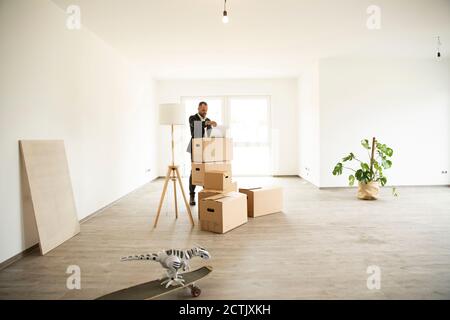 Uomo d'affari che usa il laptop sulla scatola mentre si sta in piedi in nuovo non ammobiliato appartamento Foto Stock