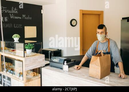 Giovane uomo con maschera protettiva in caffè in attesa di consegna uomo Foto Stock