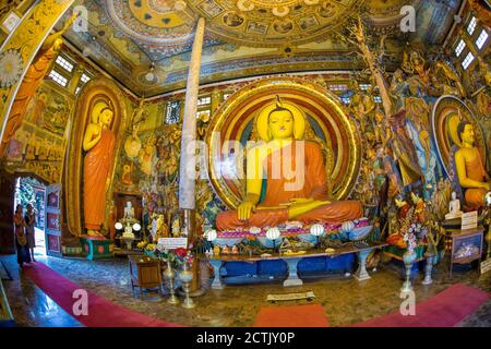 Statue di Buddha nel tempio di Gangaramaya, uno dei templi più importanti di Colombo, Sri Lanka. Le statue sono circondate da lampade e offerte. Foto Stock