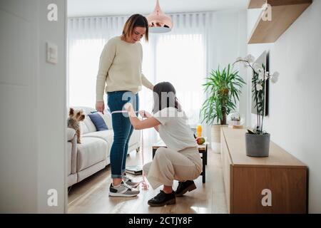 Donna che misura la coscia dell'amico con il nastro di misurazione a casa Foto Stock