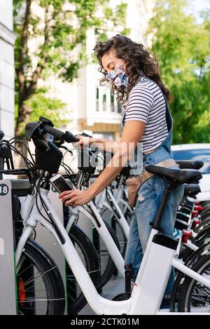 Donna che scannerizza il codice QR su bicicletta elettrica con smartphone in città Foto Stock