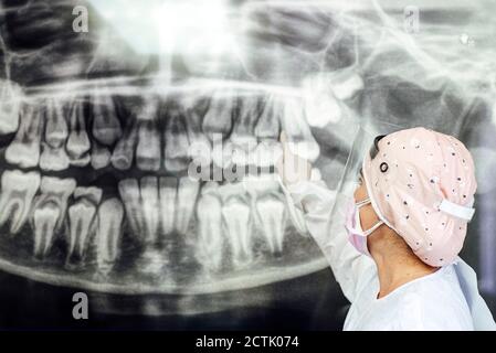 Dentista in indumenti da lavoro protettivi che punta ai raggi X dentali mentre si è in piedi in clinica Foto Stock