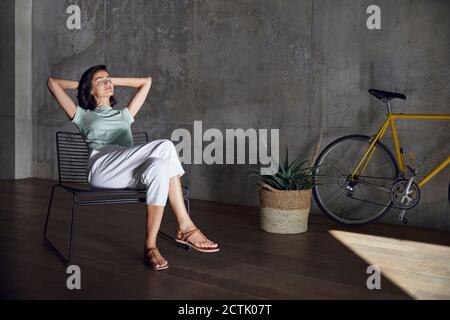 Donna imprenditore con gli occhi chiusi poggiando sulla sedia contro il muro in ufficio Foto Stock