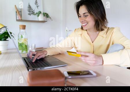 Sorridente bella giovane donna godendo di shopping online attraverso il computer portatile a. casa Foto Stock