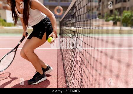 Tennista femminile che tiene racchetta e palla mentre si sta in piedi rete in tribunale Foto Stock