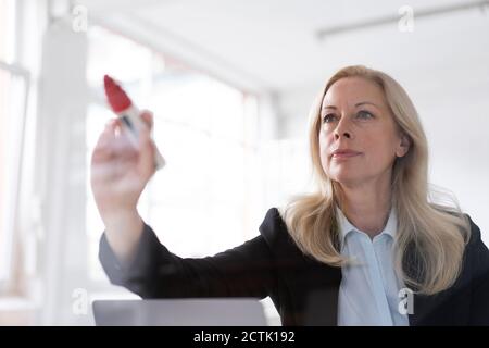 Donna imprenditore che scrive sulla finestra con pennarello in feltro l'ufficio domestico visto attraverso il vetro Foto Stock