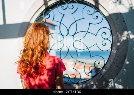 Giovane donna che ammira la vista attraverso la finestra circolare ad Alfama, Lisbona, Portogallo Foto Stock