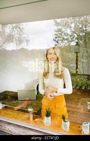 Sorridente imprenditore femminile in carica visto attraverso la finestra Foto Stock