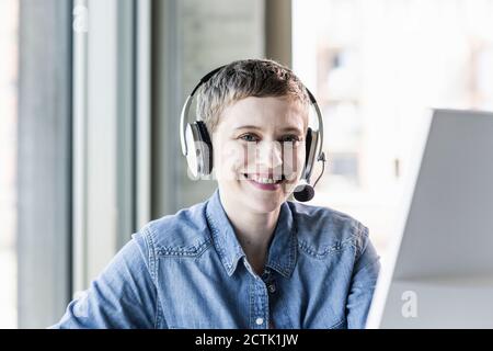 Ritratto di sorridere imprenditrice che indossa la cuffia alla scrivania in ufficio Foto Stock
