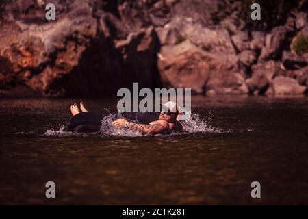 Uomo sul tubo interno che galleggia nel fiume Foto Stock