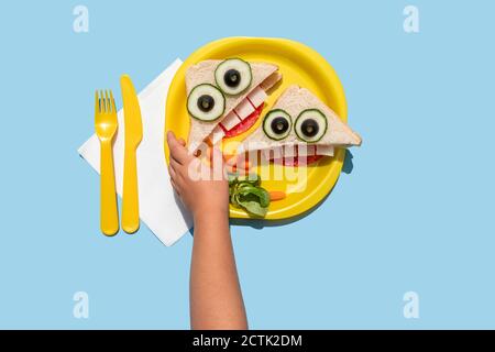 Mano della bambina che raccoglie buffo sandwich osservante con antropomorfo faccia Foto Stock