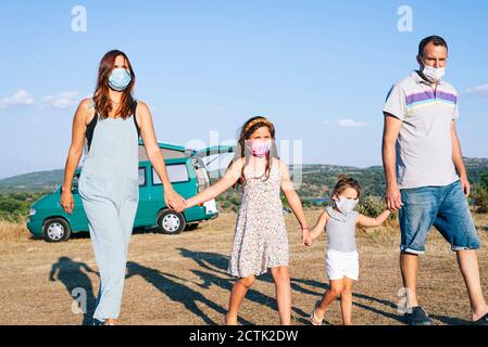 La famiglia indossa maschere che tengono le mani mentre si cammina sul paesaggio cielo Foto Stock