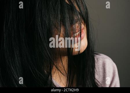 Primo piano di donna con i capelli neri e disordinati contro la parete Foto Stock