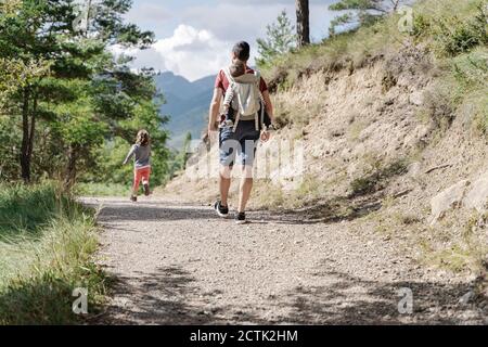 Padre camminando con i suoi figli, portando il figlio sulla schiena mentre la figlia è in corsa Foto Stock