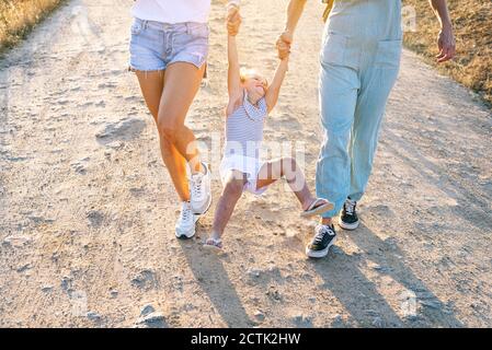 I genitori che tengono le mani della figlia mentre camminano sulla terra Foto Stock