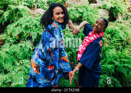 Sorridendo gli amici che fanno il cuore con la mano mentre si levano in piedi contro le piante al parco Foto Stock