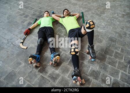 Padre stanco e figlio che si stendeva sul pavimento dopo aver praticato il rullo hockey al campo Foto Stock
