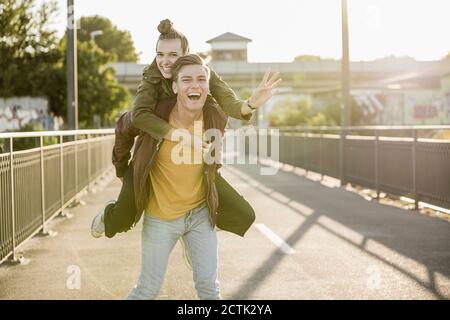 Allegro giovane uomo piggybacking ragazza in città il giorno di sole Foto Stock