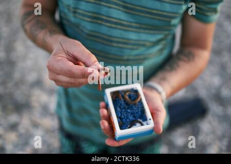 Primo piano di un adulto medio che tiene esche di pesca in spiaggia Foto Stock