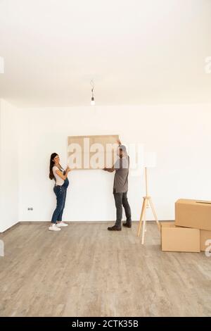 Donna incinta con il marito che porta il telaio della finestra mentre si trova in piedi nuova casa Foto Stock