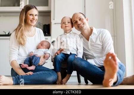 Sorridi i genitori che tengono i bambini mentre si siedono sul pavimento a. casa Foto Stock