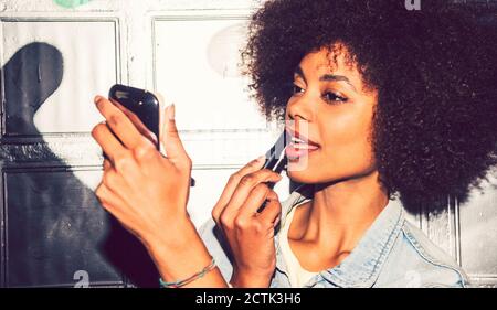 Primo piano della donna con capelli ricci che applicano il rossetto mentre si guarda nello specchio di notte Foto Stock