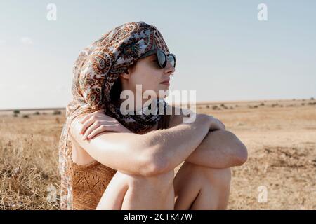 Ritratto di giovane donna che indossa foulard e occhiali da sole seduti all'aperto con croce braccia Foto Stock