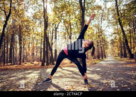 Giovane femmina jogger che allunga la gamba nella foresta d'autunno Foto Stock