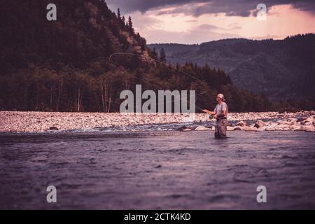 Volare pescatore casting con canna da pesca in piedi nel fiume Foto Stock