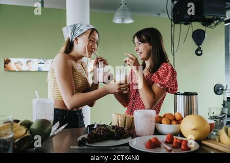 Ragazze adolescenti in piedi in cucina bevendo frullati di frutta fresca con cannucce da bere